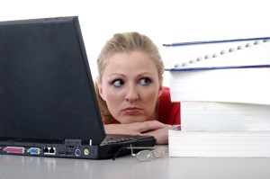 Photo of a pile of reference books, a laptop and a daunted woman.